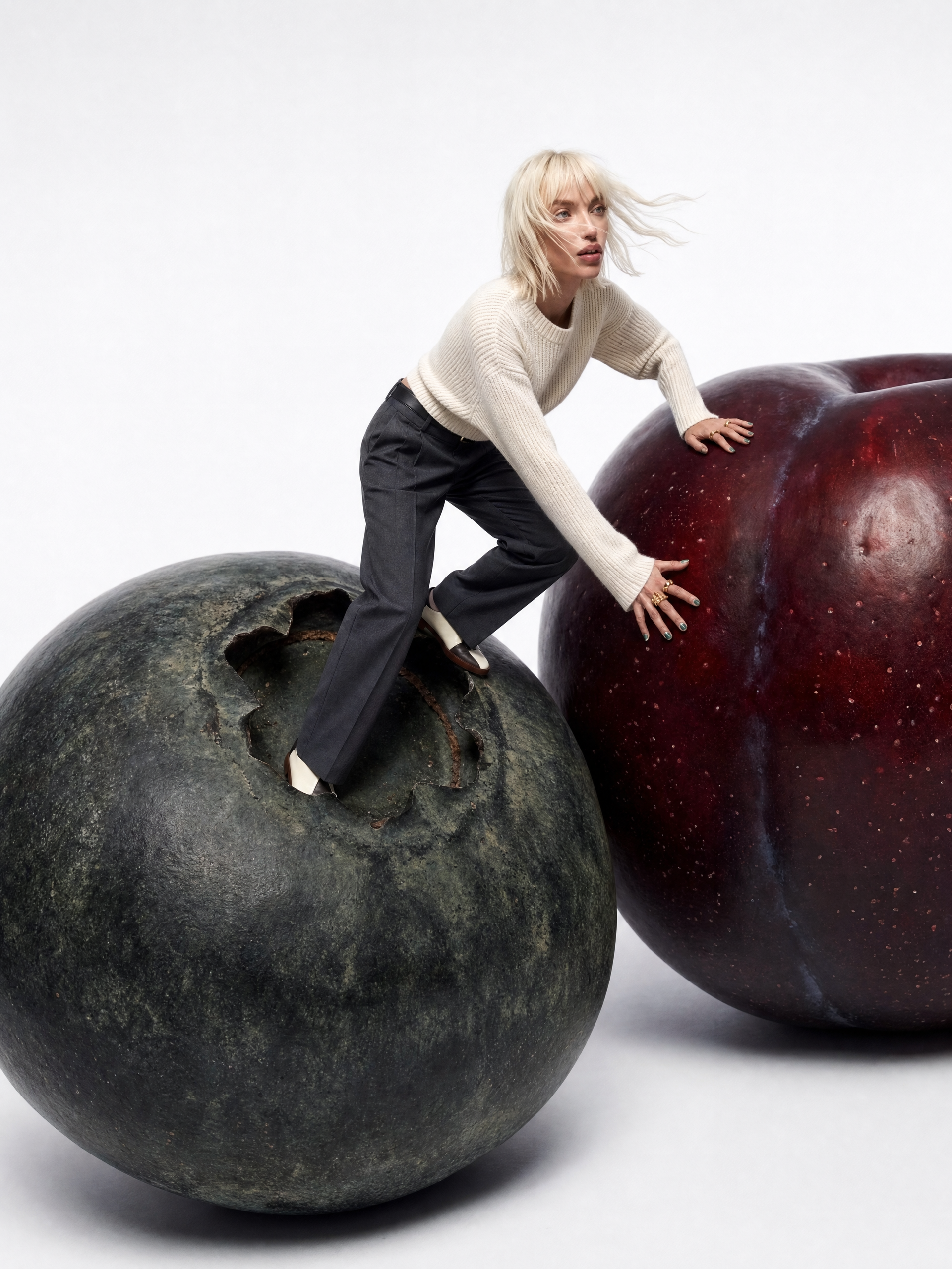 Blonde woman balancing between giant green and dark plums