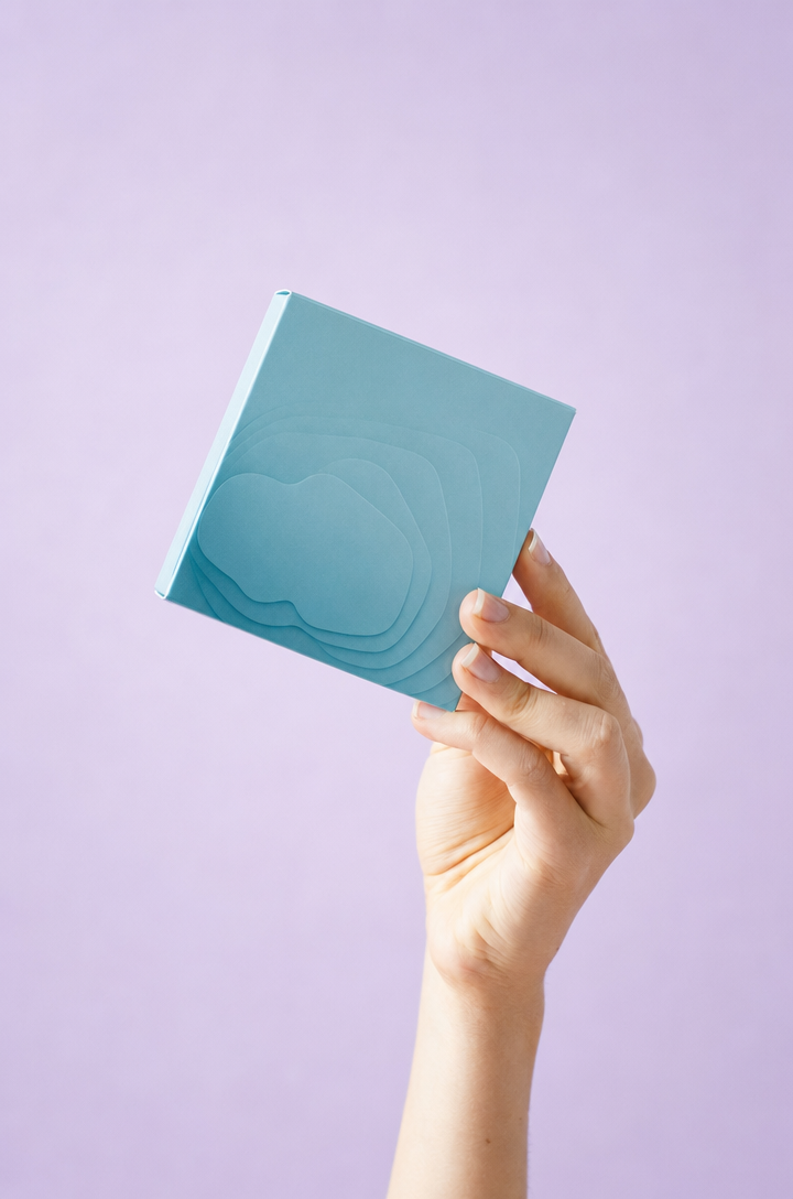 Hand holding teal-blue skincare mask box, lavender background