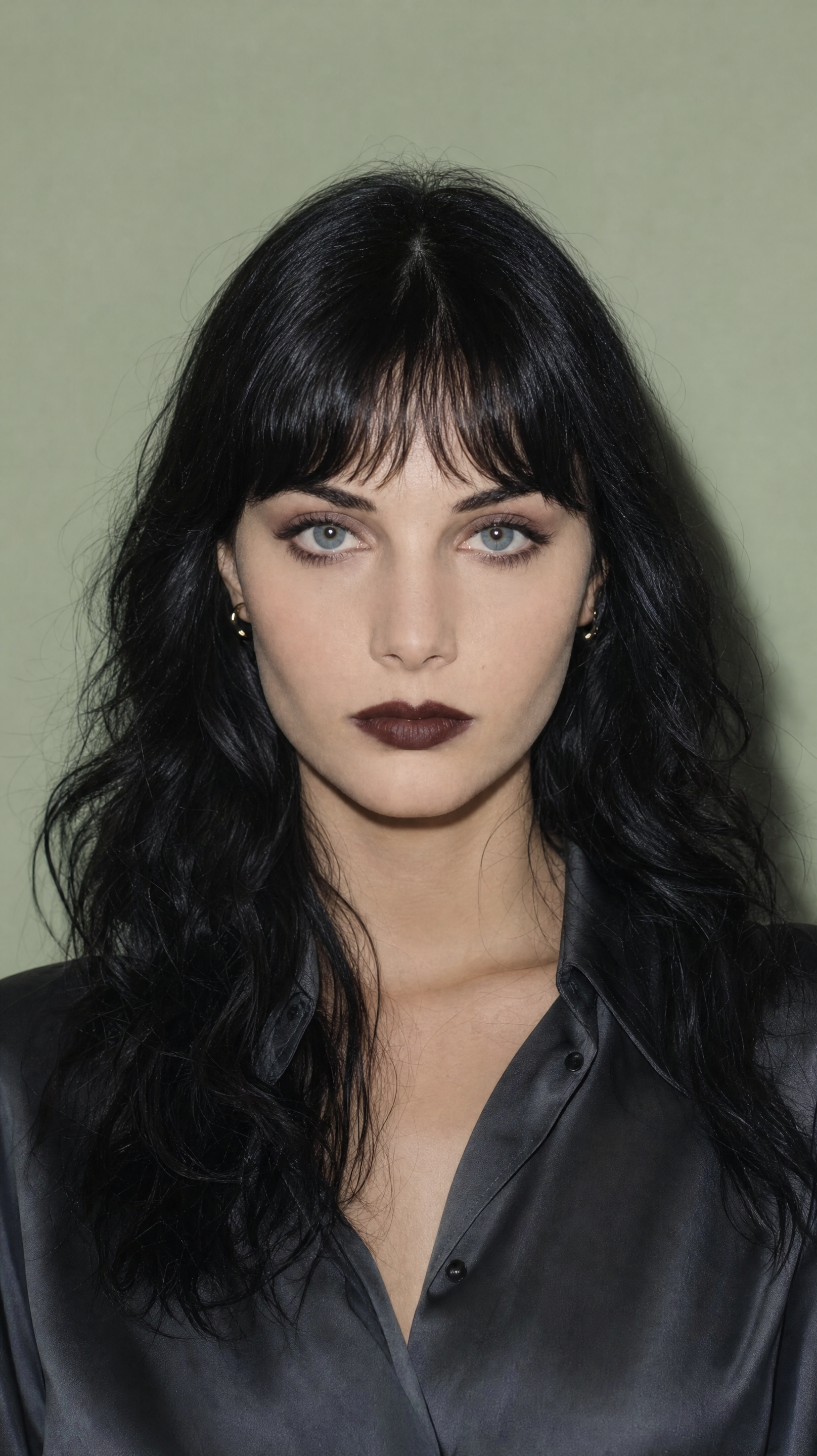 Pale woman with wavy black hair, sage backdrop
